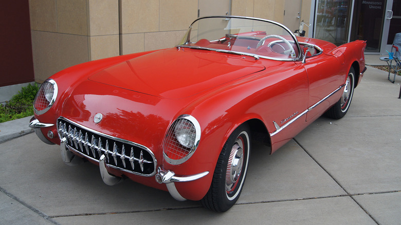 Red 1954 Corvette convertible parked on walkway outside dealership