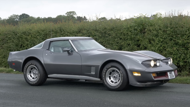 Grey 1981 Corvette parked on asphalt in front of tall hedgerow