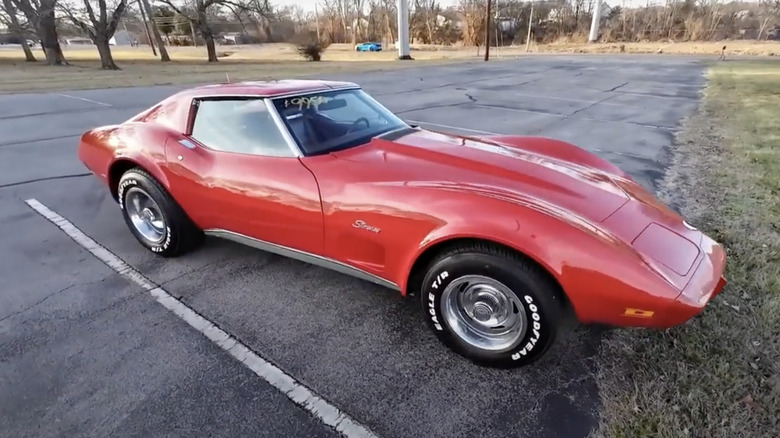 Red 1975 Corvette parked in lot with nose poking onto grass field