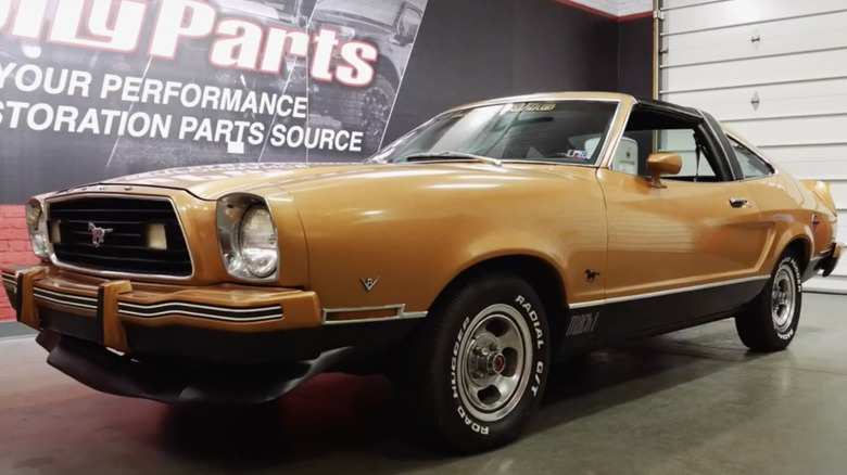 Gold Mustang II Mach I parked in garage with CJ Pony Parts banner on wall behind