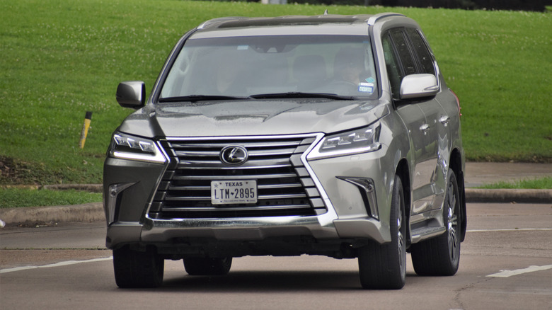 A silver Lexus LX570 is driving down a road.