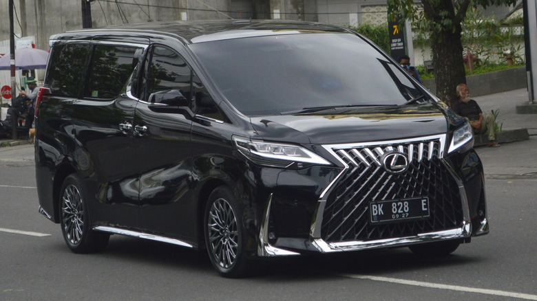 A black Lexus LM is driving on a street.