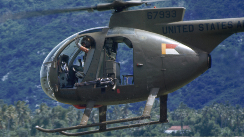 A Hughes OH-6 Cayuse flying low to the ground with pilot waving