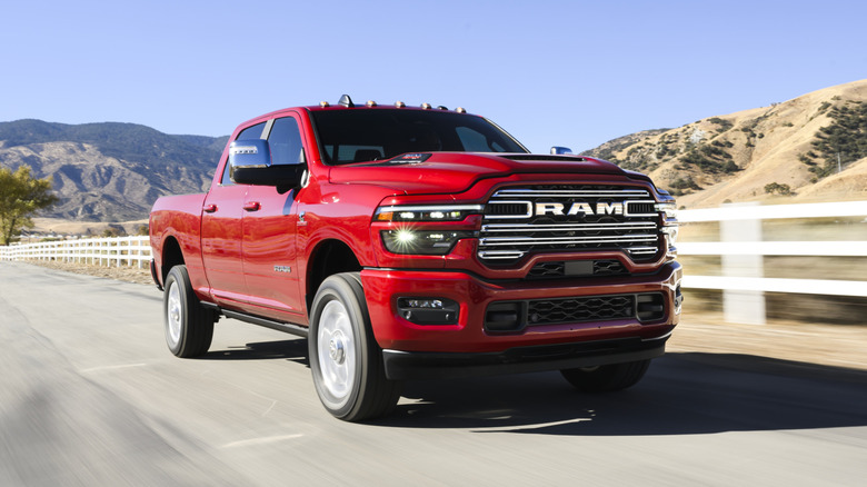 2025 Ram 2500 Heavy Duty Laramie driving on a paved road with mountains and a white fence in the background