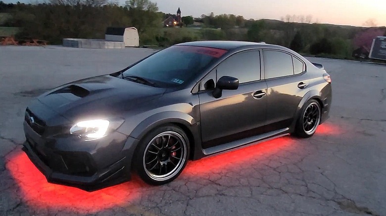 Red underglow lighting comes from a black car sitting on cracked asphalt