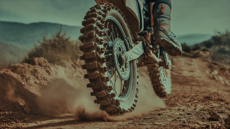 Rear wheel of a motocross motorcycle kicking up dust on an off-road trail