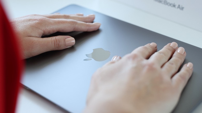  Woman hand rests on top cover of Apple Macbook Air.