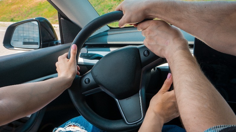 two people turning steering wheel