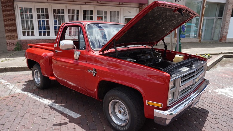 Red 1986 Chevy square body truck on display parked on a brick street.