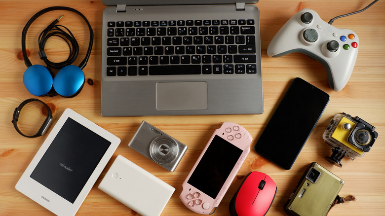 Used electronics, including a laptop, smartphone, eReader and gaming system controller, displayed on a wooden surface