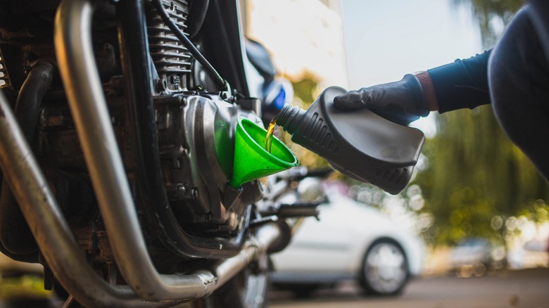 Person adding oil to motorcycle