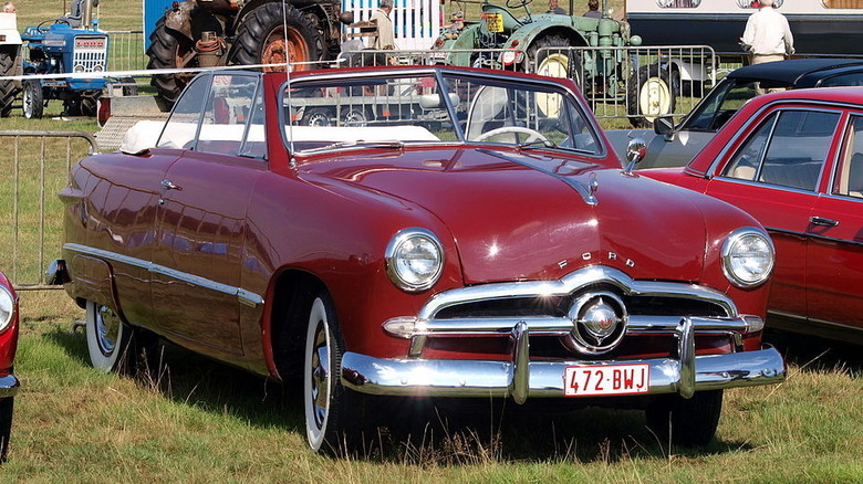 A red 1949 Ford Custom convertible parked in a grass field