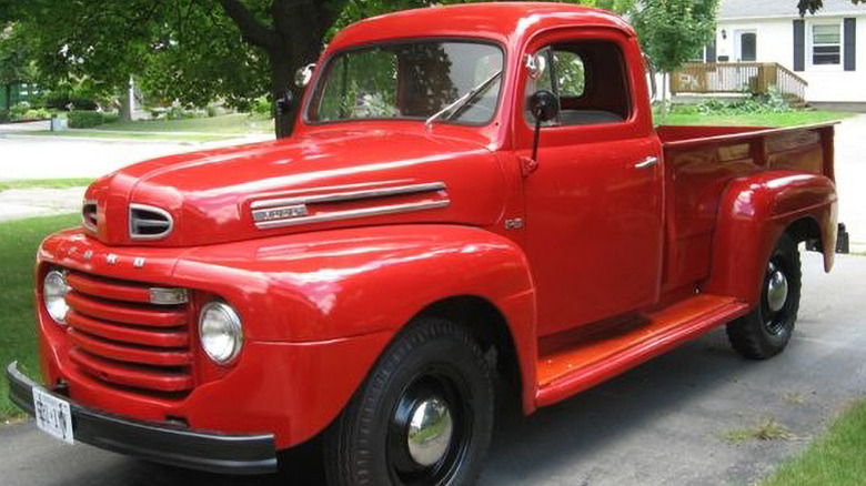 A red 1950 Ford F3 pickup parked in a suburban driveway.