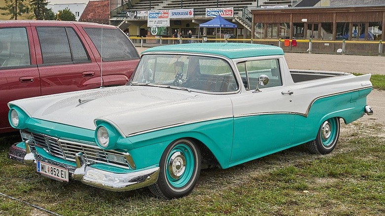 A teal and white 1957 Ford Ranchero parked in a grass lot.