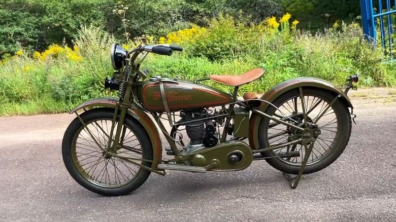 A green 1927 Harley-Davidson BA parked beside bushes