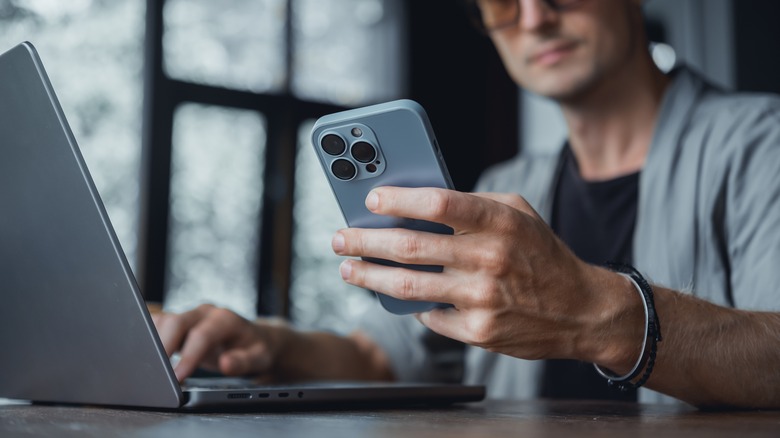 person holding iPhone and typing on laptop