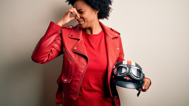 woman holding nose while holding motorcycle helmet