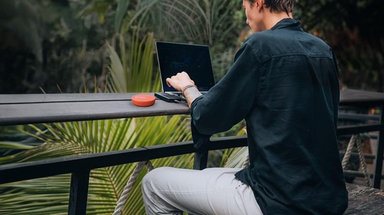 Man working on a laptop outside with a mobile hotspot on the table