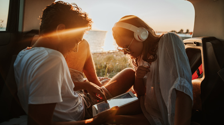 young couple camping in back of van with laptop and headphones