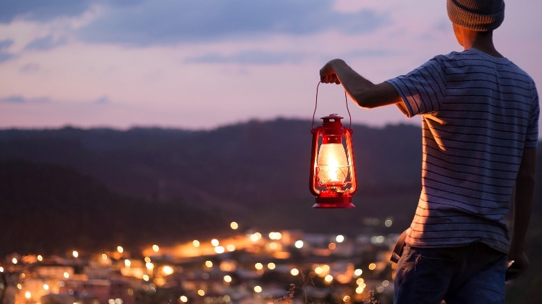 Man holding lantern looking at city lights