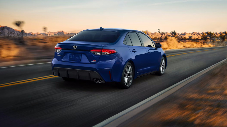 Blue Toyota Corolla hybrid driving away from camera on desert highway with sun setting in sky