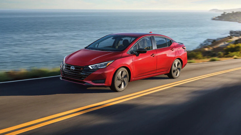 Red Nissan Versa driving on coastal highway with ocean in background