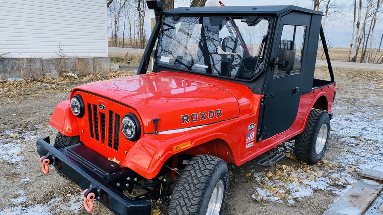 Red Mahindra Roxor parked in dirt lot with light snowfall