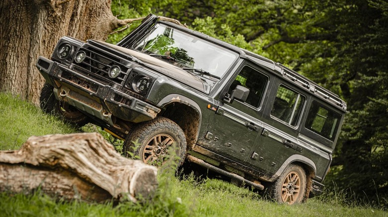 Green Ineos Grenadier  driving through woods with mud on wheels and body