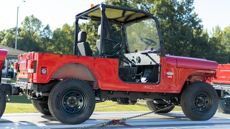 Red Mahindra Roxor parked on flatbed trailer with trees in background