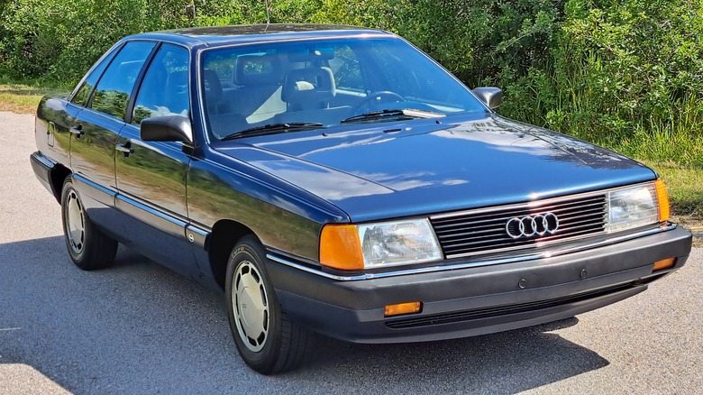 A dark blue Audi 5000 sedan parked on asphalt in front of trees and grass