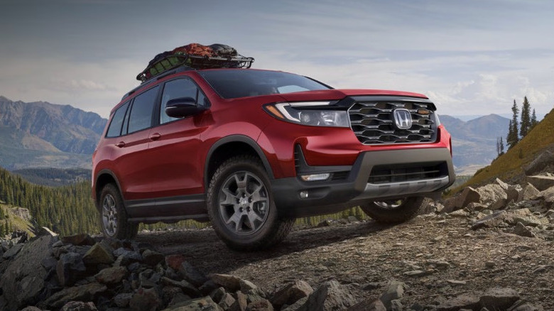 Red Honda Passport with camping gear on roof rack climbing rocky mountain road