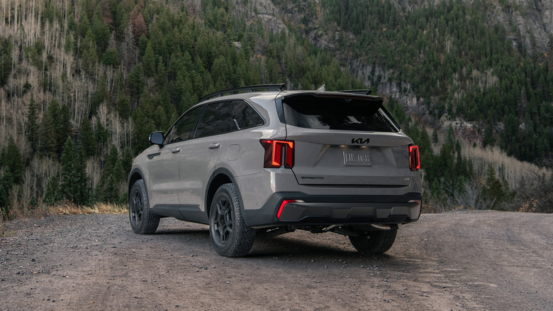 Grey Kia Sorento on unpaved mountain road among trees