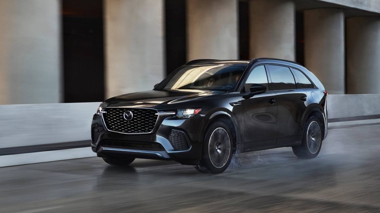 Black Mazda CX-70 SUV driving on city street in front of grey cement pillars