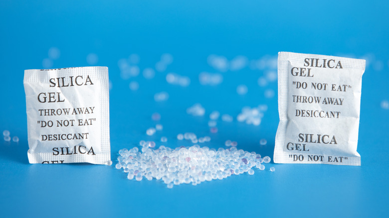 Two silica gel packets and silica beads with a blue background