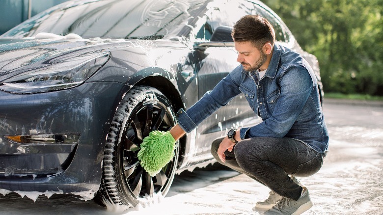 A man using mitts to clean the car wheels