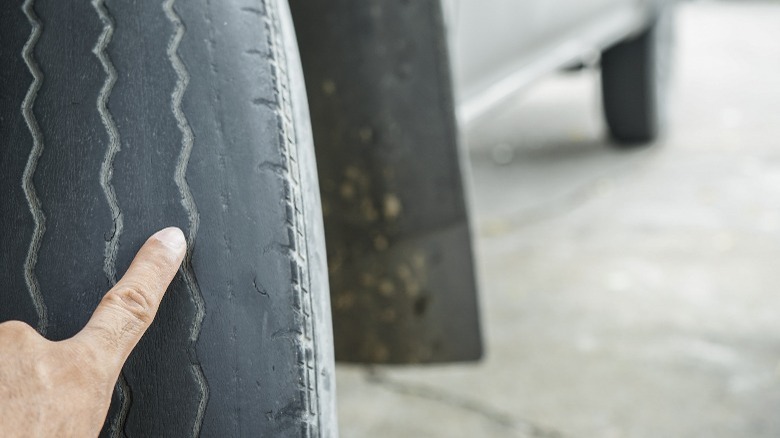 A hand pointing at a worn tire