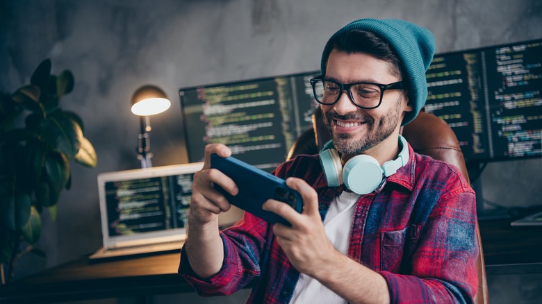 man, wearing headphones around neck, playing games on mobile