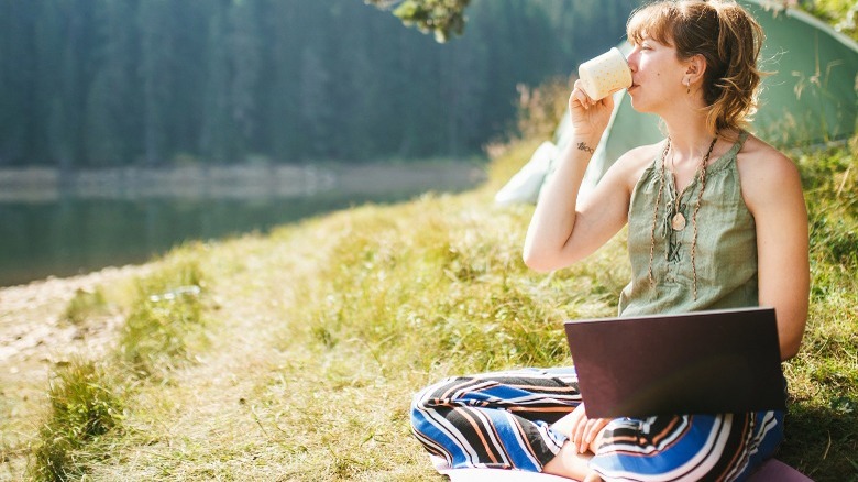 Woman driving coffee sitting in the grass near a river