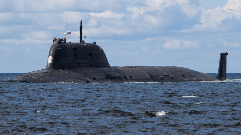 A Yasen-M submarine sailing along the surface of the ocean with crew members on its mast.