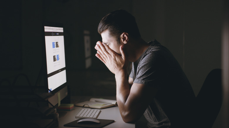 Man rubbing eyes at computer