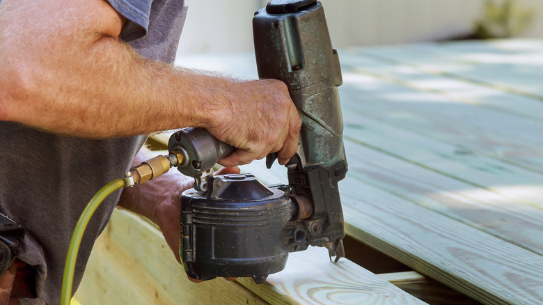 A man using a nail gun on a wooden plank.