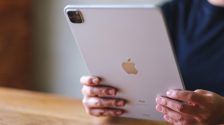 A person holding iPad on wooden desk