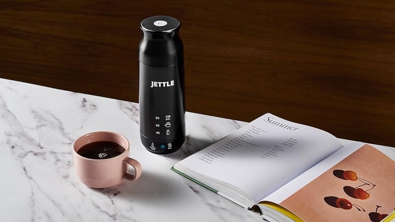 A coffee cup, a book, and a portable kettle sitting on a table