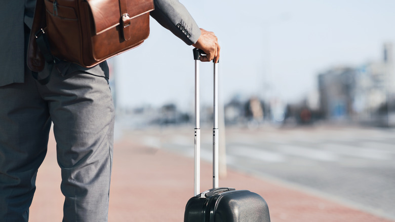 A business man traveling with a rolling suitcase.