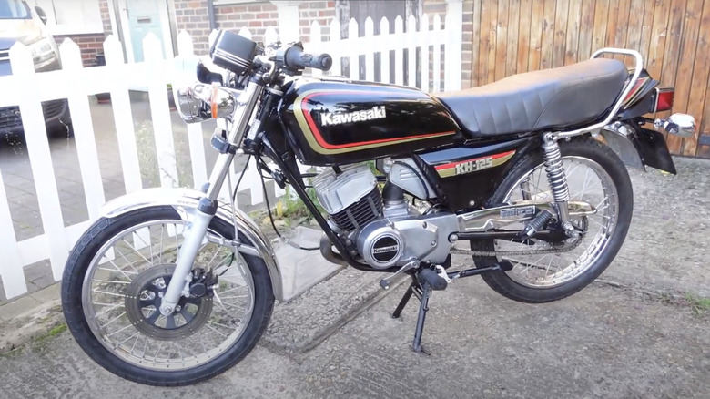 Kawasaki KH125 motorcycle parked in driveway with white picket fence in background