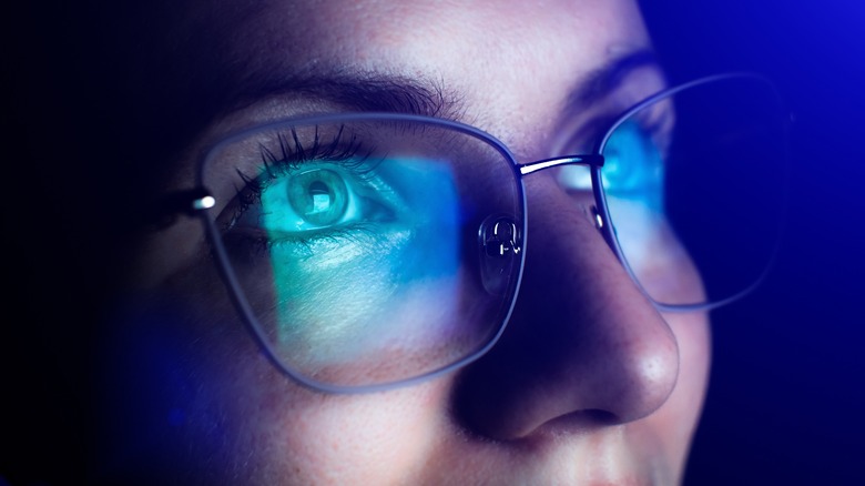 monitor with blue light reflected in woman's eyeglasses