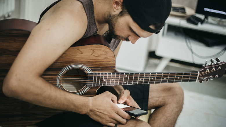 man using phone holding guitar