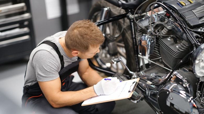 person writing on paper looking at their motorcycle