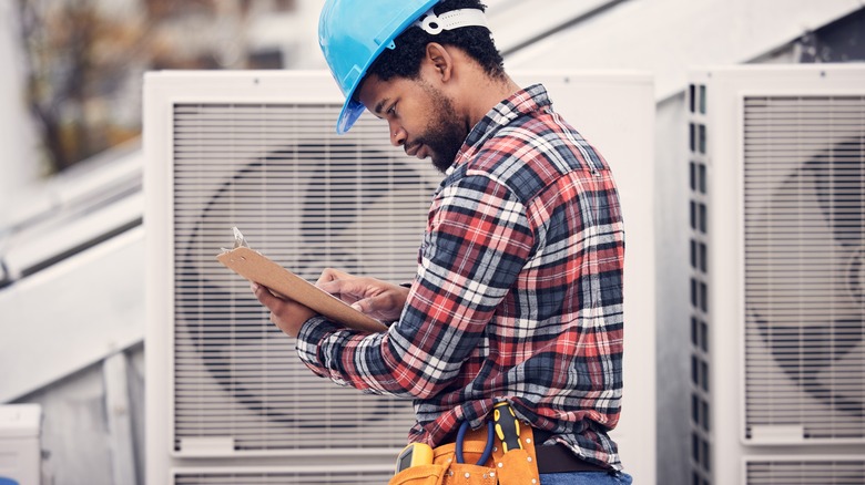 Repair person in a hard hat looking at a clipboard