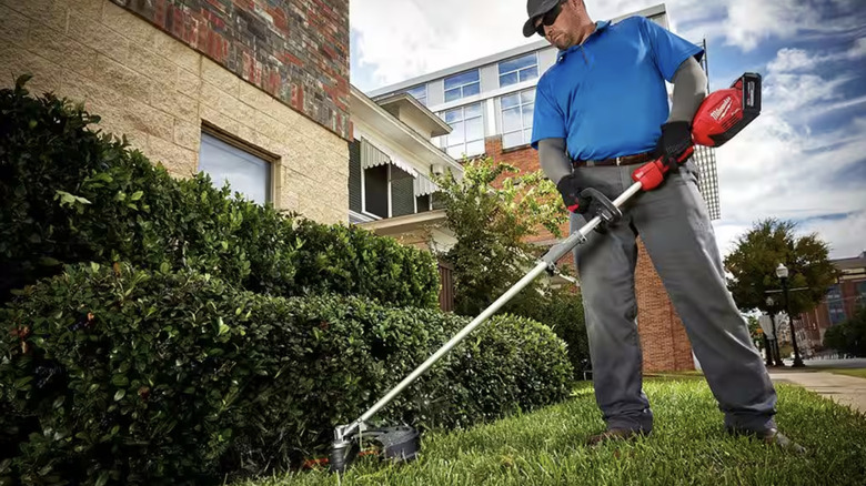 Man using a string Milwaukee trimmer to cut grass